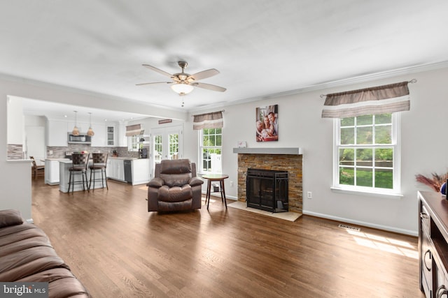 living room with crown molding, ceiling fan, visible vents, a fireplace, and wood finished floors