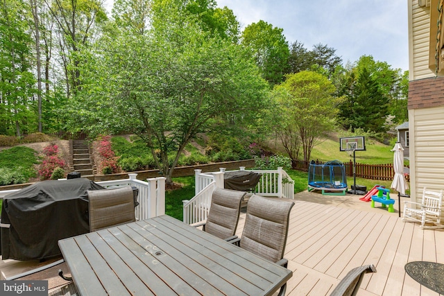 wooden deck with a trampoline, fence, outdoor dining area, and stairway