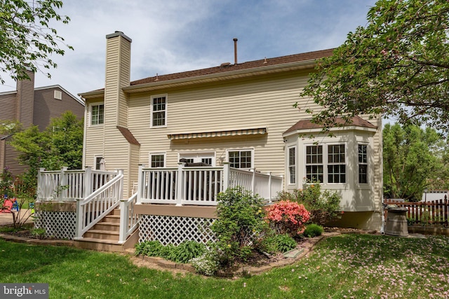back of property featuring fence, a deck, a yard, and a chimney