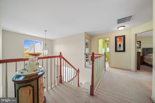 hallway with visible vents, baseboards, light carpet, and an upstairs landing