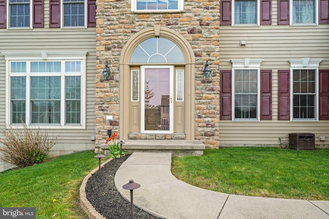 entrance to property with a lawn, central air condition unit, and stone siding