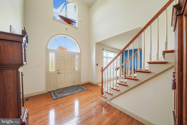 foyer entrance featuring baseboards, a high ceiling, wood-type flooring, and stairs
