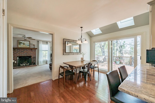 dining area featuring a fireplace, a healthy amount of sunlight, lofted ceiling with skylight, and dark wood-type flooring