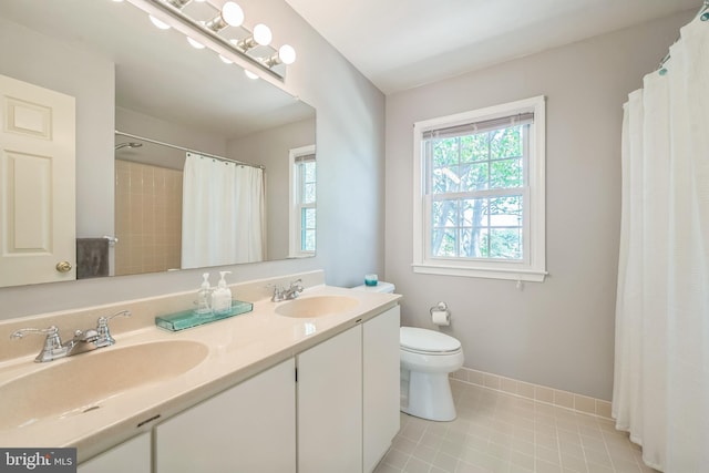bathroom with double vanity, toilet, baseboards, and a sink