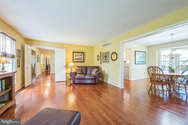 living area featuring hardwood / wood-style floors, visible vents, a notable chandelier, and baseboards