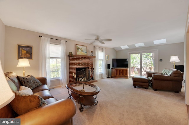 living area with a fireplace, ceiling fan, carpet flooring, and a skylight