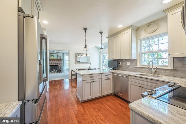 kitchen with tasteful backsplash, a sink, appliances with stainless steel finishes, light wood-type flooring, and a peninsula