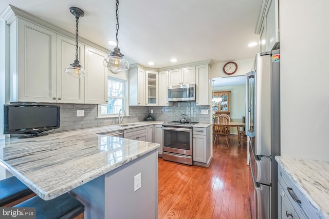 kitchen with decorative backsplash, stainless steel appliances, light wood-style floors, a sink, and a peninsula