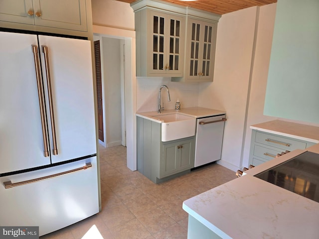 kitchen with a sink, light tile patterned floors, glass insert cabinets, dishwashing machine, and freestanding refrigerator