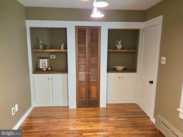 unfurnished dining area with baseboards, built in shelves, wood finished floors, and a baseboard heating unit