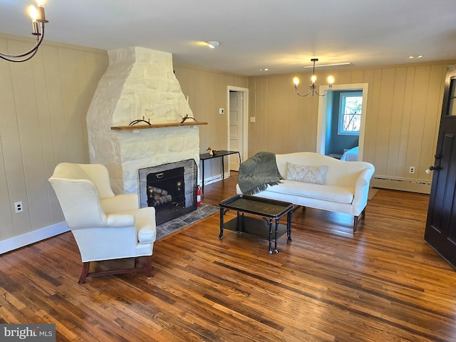 living area with baseboard heating, baseboards, an inviting chandelier, wood finished floors, and a stone fireplace