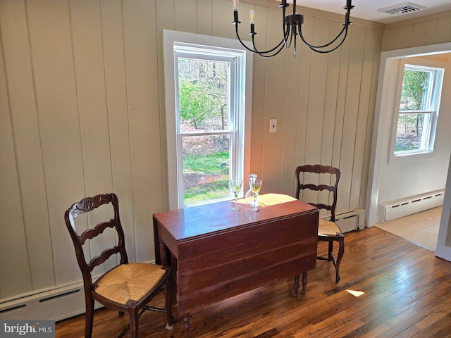 dining space with baseboard heating, visible vents, hardwood / wood-style flooring, and an inviting chandelier