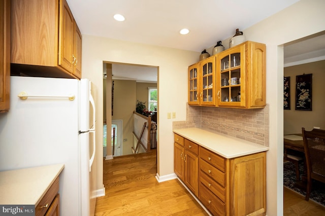 kitchen featuring freestanding refrigerator, light wood-style flooring, backsplash, glass insert cabinets, and light countertops