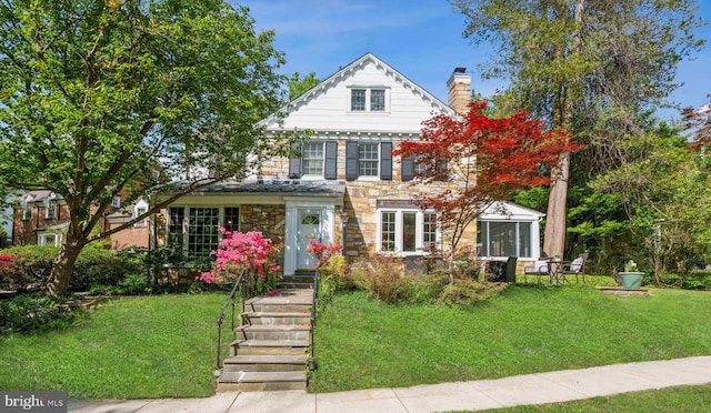 view of front of property featuring a sunroom, a chimney, stone siding, and a front lawn