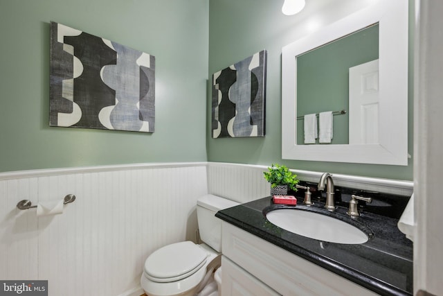 half bath with toilet, wainscoting, and vanity