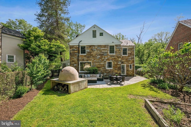 rear view of house with outdoor lounge area, fence, stone siding, a patio, and a yard