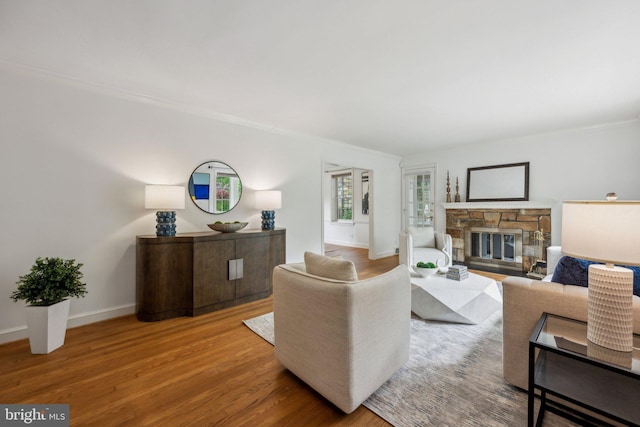 living area featuring crown molding, wood finished floors, and a stone fireplace