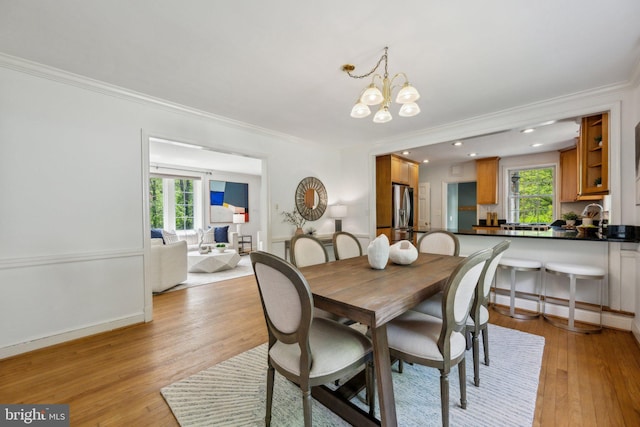 dining room with light wood-type flooring, an inviting chandelier, ornamental molding, and plenty of natural light