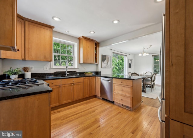 kitchen with a peninsula, a healthy amount of sunlight, light wood-style floors, a sink, and appliances with stainless steel finishes