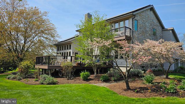 rear view of house with a deck, a chimney, a yard, stone siding, and a balcony