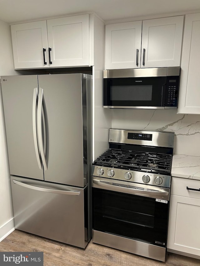 kitchen with appliances with stainless steel finishes, white cabinetry, light wood-style flooring, light stone countertops, and backsplash