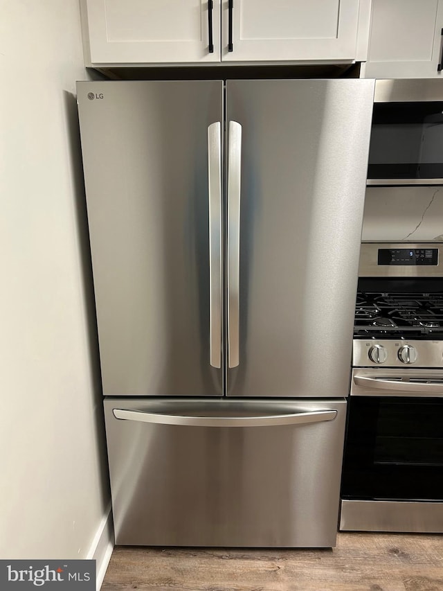 kitchen view of stainless steel appliances, light wood-style floors, and white cabinetry