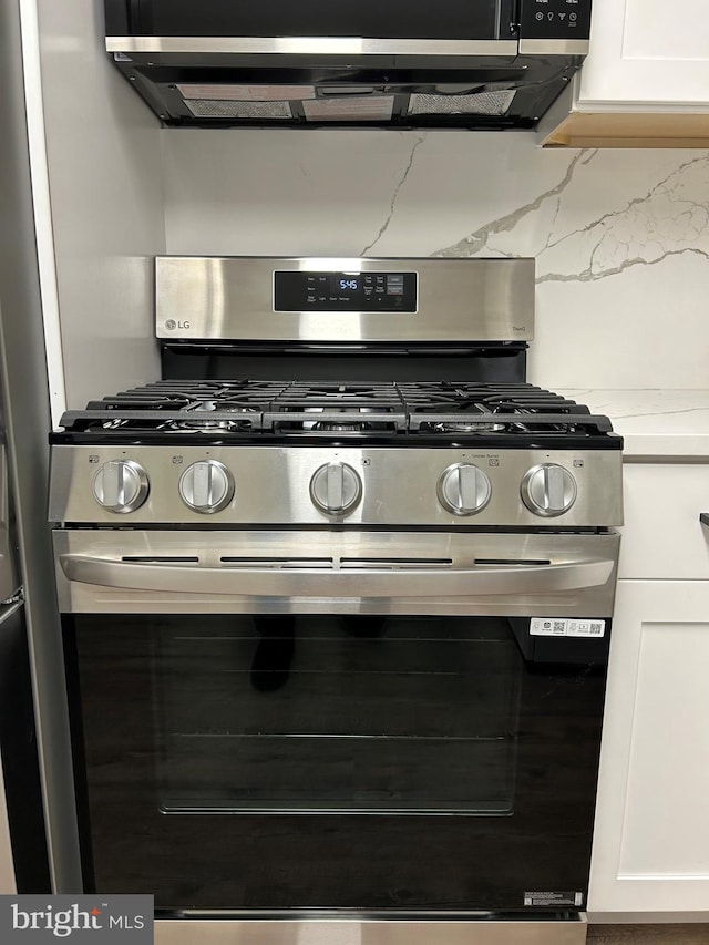 kitchen view of gas stove, white cabinetry, and light countertops