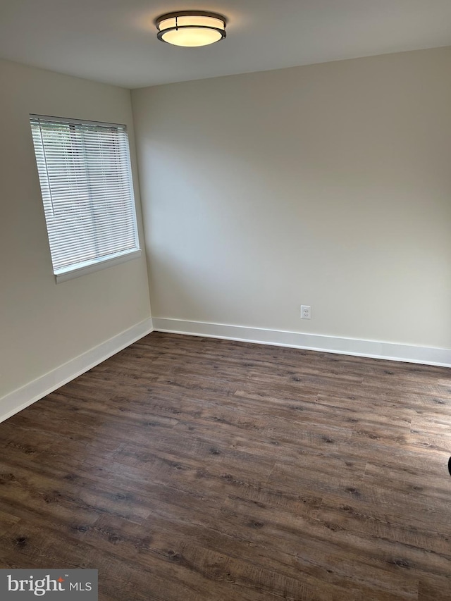 unfurnished room featuring baseboards and dark wood-type flooring