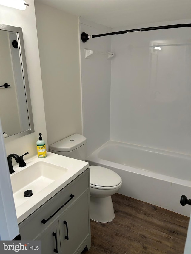 bathroom featuring wood finished floors, toilet, vanity, and tub / shower combination
