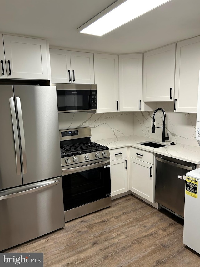kitchen with stainless steel appliances, a sink, white cabinetry, light stone counters, and backsplash
