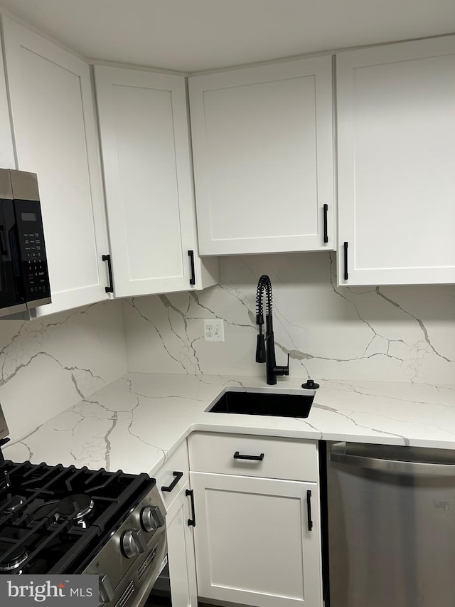 kitchen with appliances with stainless steel finishes, white cabinets, a sink, and decorative backsplash
