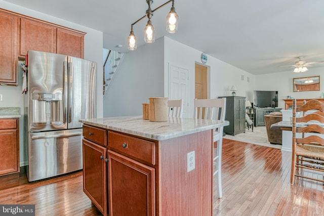 kitchen with a ceiling fan, stainless steel refrigerator with ice dispenser, light wood-type flooring, open floor plan, and a breakfast bar