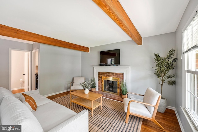 living area with baseboards, a brick fireplace, beam ceiling, and wood finished floors