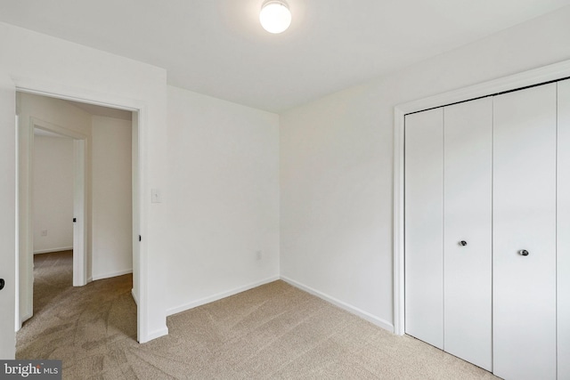 unfurnished bedroom with baseboards, a closet, and light colored carpet