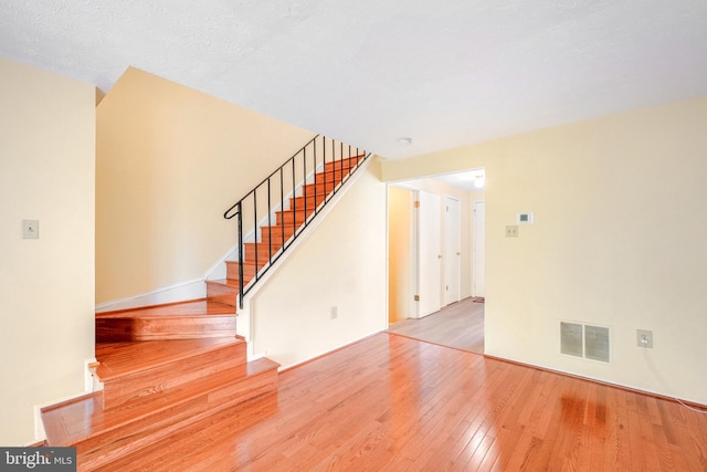 unfurnished living room with hardwood / wood-style flooring, stairs, and visible vents