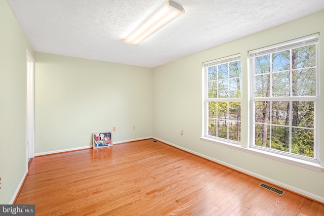unfurnished room with baseboards, a textured ceiling, light wood-style flooring, and visible vents