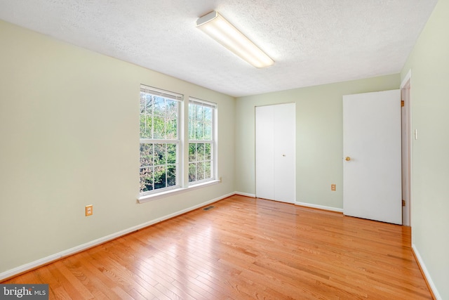 spare room featuring a textured ceiling, visible vents, baseboards, and light wood finished floors