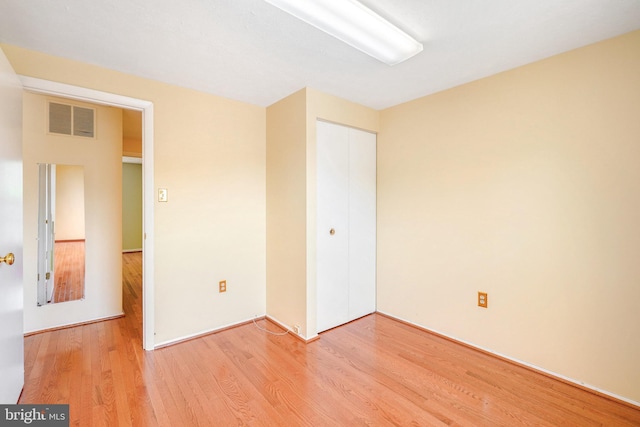 unfurnished bedroom with visible vents, wood finished floors, and a closet