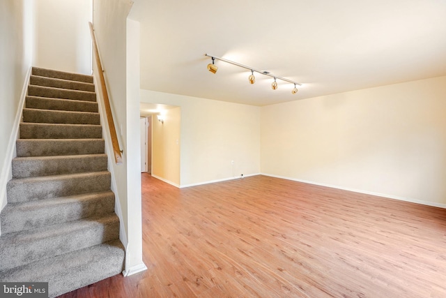 stairs featuring baseboards, rail lighting, and wood finished floors