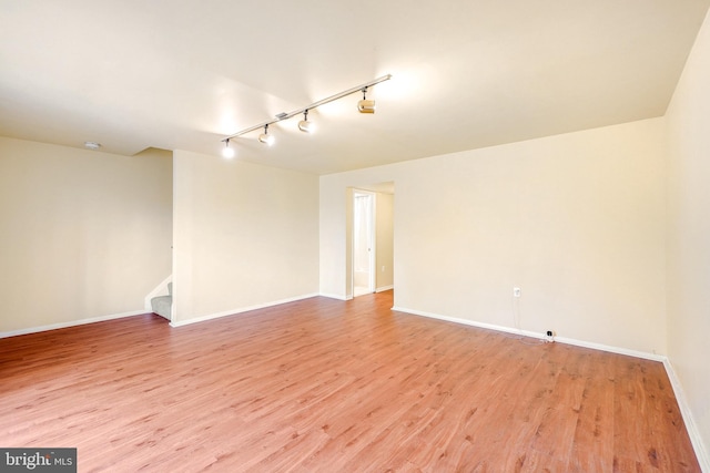 empty room with baseboards, rail lighting, light wood-style flooring, and stairway