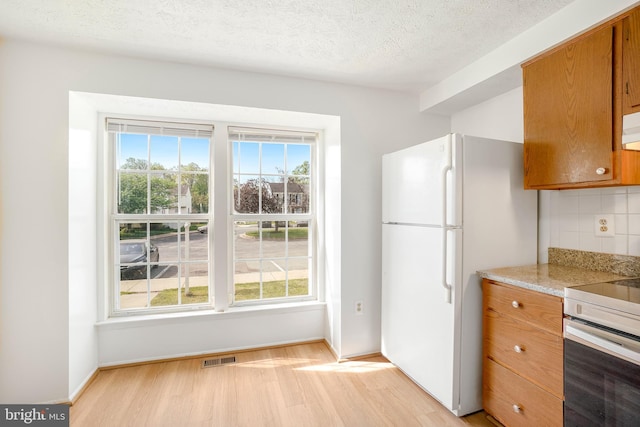 kitchen with decorative backsplash, brown cabinets, freestanding refrigerator, light wood finished floors, and electric stove