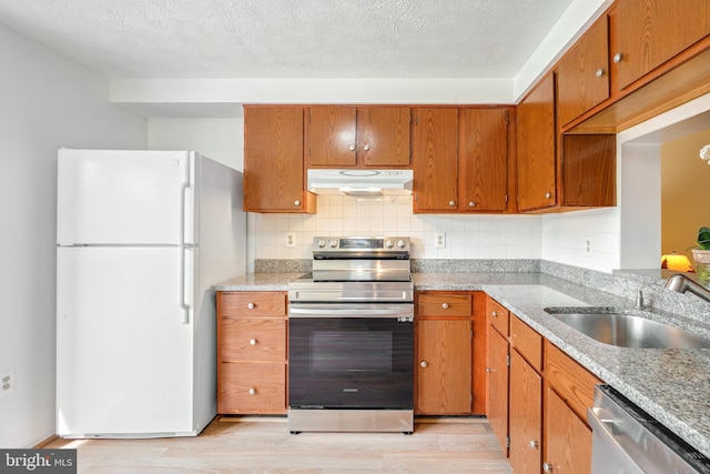 kitchen featuring brown cabinets, a sink, light wood finished floors, stainless steel appliances, and under cabinet range hood