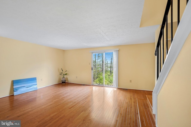 empty room with light wood-type flooring, a textured ceiling, baseboards, and visible vents
