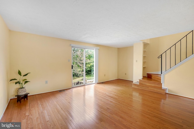 unfurnished living room featuring wood-type flooring, baseboards, visible vents, and stairway