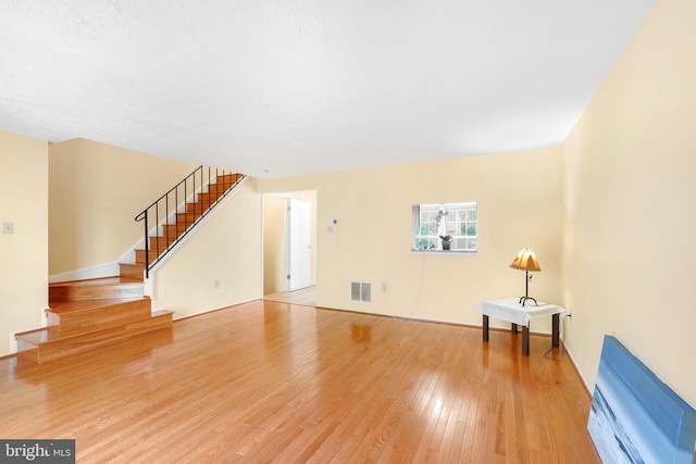 unfurnished living room featuring stairway, light wood finished floors, and visible vents