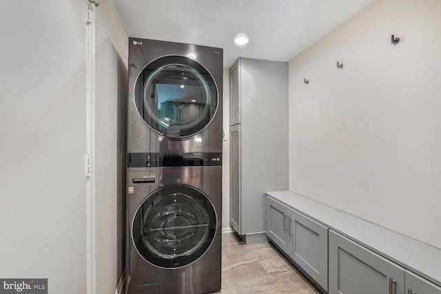 laundry area featuring cabinet space, baseboards, and stacked washer / dryer