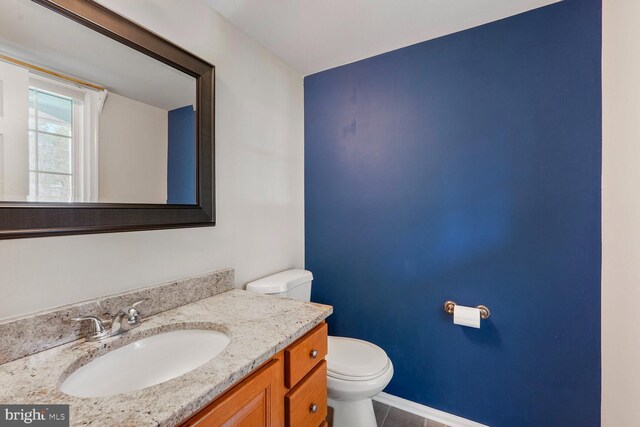 half bath with vanity, tile patterned flooring, baseboards, and toilet