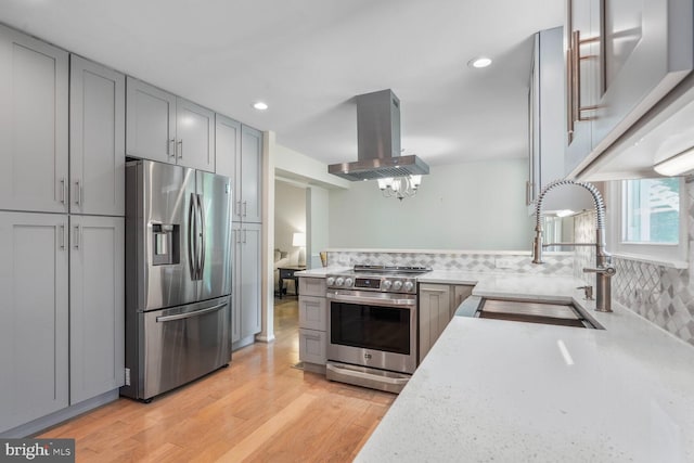 kitchen with appliances with stainless steel finishes, a sink, light wood finished floors, island exhaust hood, and gray cabinetry