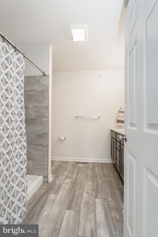 bathroom with vanity, tiled shower, wood finished floors, and baseboards