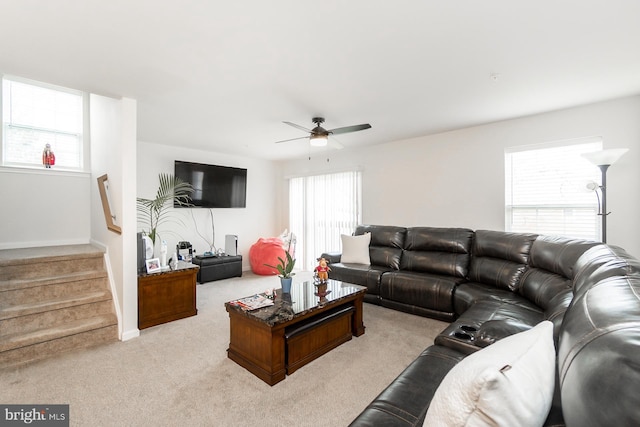 living room with baseboards, stairway, a ceiling fan, and light colored carpet